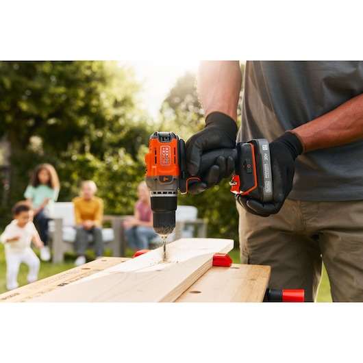BLACKDECKER BCD383D1 cordless drill in use on wood outdoors, close-up showing black and orange design.