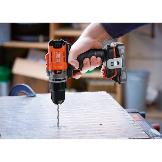 BLACK+DECKER BCD383D1 cordless drill in use, drilling into a metal sheet, close-up view of drill and hand.