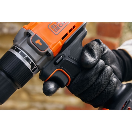 Photo of BLACKDECKER BCD383D1 cordless drill being gripped by a gloved hand, focus on trigger and handle.