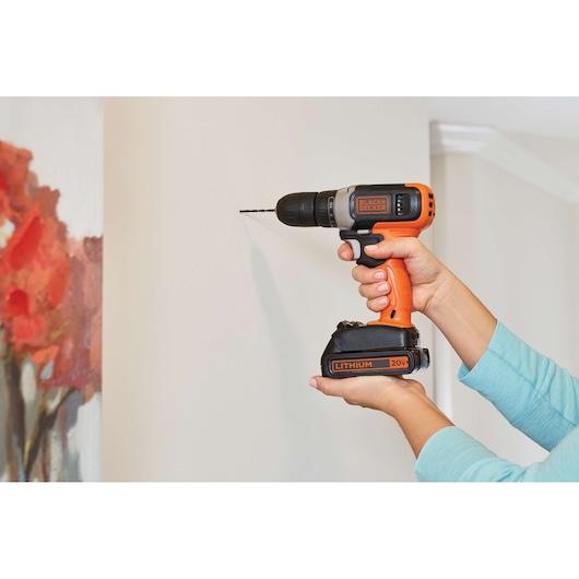 Photo of BLACKDECKER cordless drill BCD70250PK in use on wall, orange and black, 20V lithium battery visible.