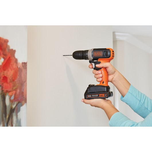 Photo of BLACKDECKER cordless drill BCD702C1 held against a wall, side view, orange and black power tool.