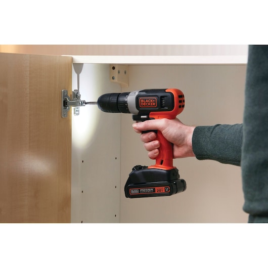 BLACKDECKER BCD702C1 cordless drill with orange and black body used on cabinet hinge, side angle photo.