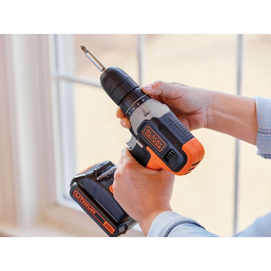 Photo of BLACK+DECKER cordless drill BCD702PK2B, 20V lithium battery, in use near a window.