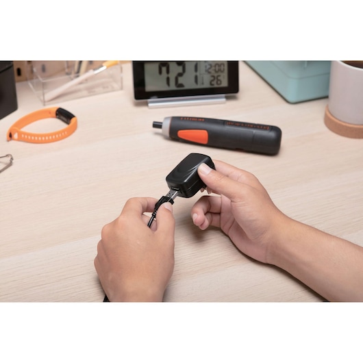 BLACKDECKER BD40K27 cordless screwdriver on desk, hand connecting charging cable, side angle