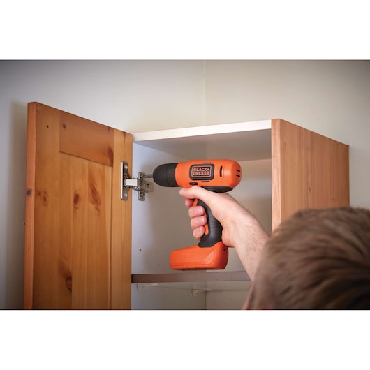 Photo of BLACKDECKER BDCD8HDPK cordless drill in use tightening hinge on wooden cabinet door.
