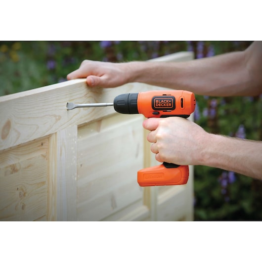 Photo of BLACK+DECKER BDCD8HDPK orange cordless drill in use on light wood outdoors.