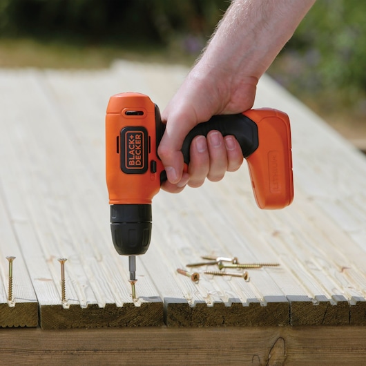 BLACKDECKER BDCD8HDPK orange cordless drill being used to drive screws into wooden planks outdoors.