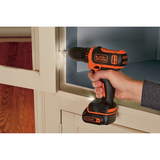 BLACK+DECKER BDCDD12C cordless drill with orange and black design being used on cabinet hinge.