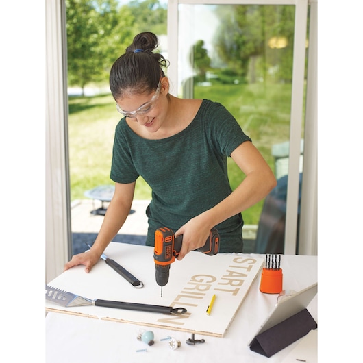 Photo of BLACKDECKER BDCDD12C cordless drill in use on a craft project with drill bits and tools on the table.