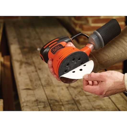Photo of BLACKDECKER BDERO100 random orbital sander with sanding pad being attached, shown in a workshop.