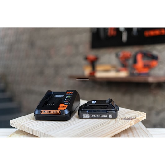Photo of BLACK+DECKER BDL2020S 20V battery charger and lithium battery on a wooden board in a workshop setting.