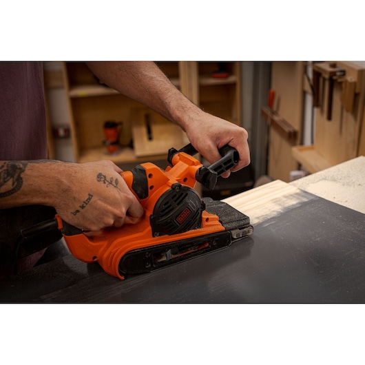 Photo of BLACK+DECKER BEBS0900 belt sander in use on a wooden surface, close-up view.