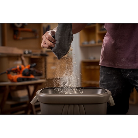 BLACKDECKER BEBS0900 sander dust bag being emptied over a bin in a workshop, orange sander in background.