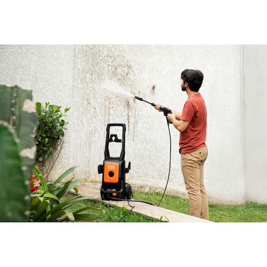 BLACKDECKER BEPW1520L pressure washer used outdoors to clean a stained wall, orange and black unit.