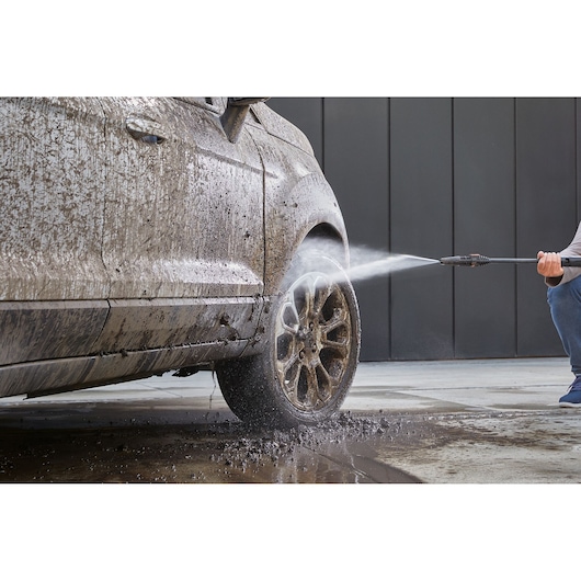 BLACKDECKER BEPW2200 pressure washer cleaning muddy car tire in action, outdoor angle.