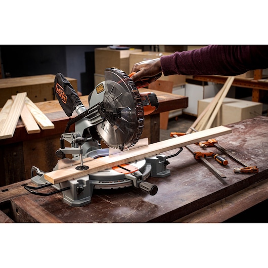 Photo of BLACKDECKER BES7101800MS miter saw cutting wood on a workbench in a workshop.