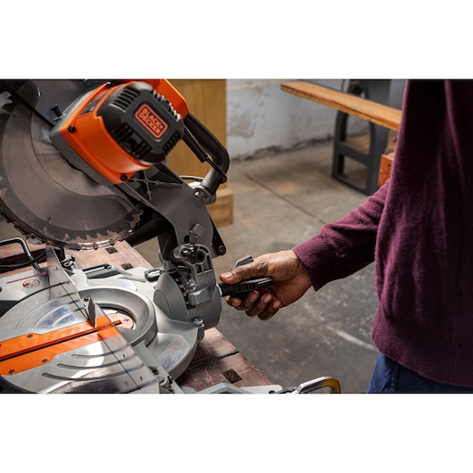 Photo of BLACKDECKER BES7101800MS miter saw in use, close up of hand adjusting angle on workbench.