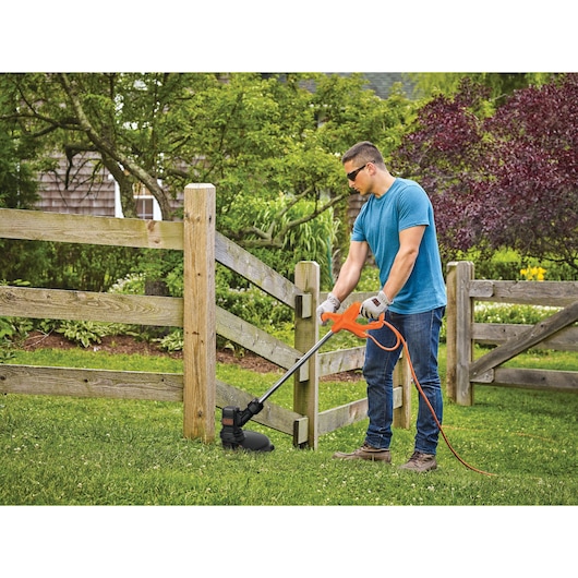 Photo of BLACKDECKER string trimmer BEST935 in use on grass near wooden fence outdoors.