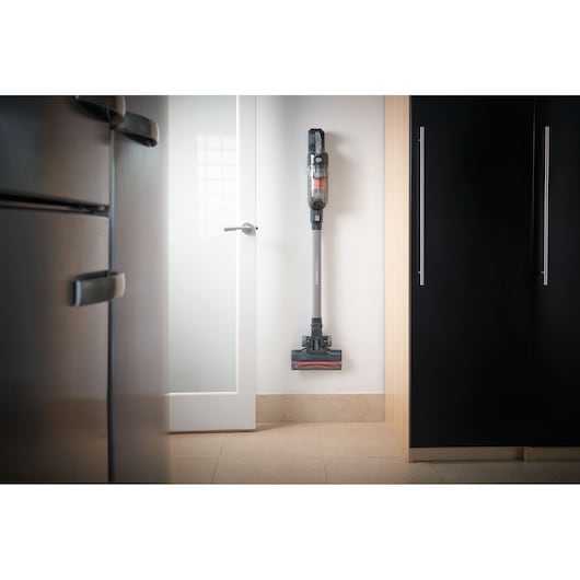 BLACKDECKER BHFEA18D1 cordless stick vacuum stored upright on a white wall in a modern kitchen.
