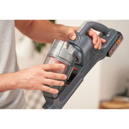 Close-up of hands removing dust container from BLACK+DECKER cordless vacuum cleaner BHFEA18D1.