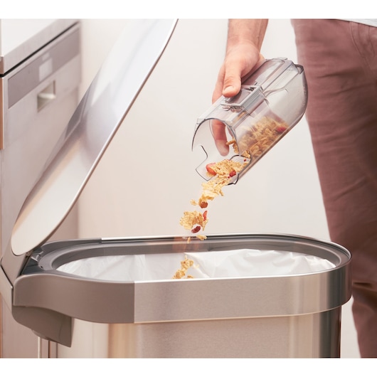 BLACKDECKER BHFEA18D1 vacuum canister being emptied into a stainless steel trash bin, close-up.