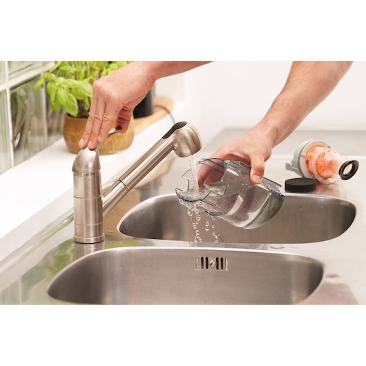 BLACKDECKER BHFEA18D1 vacuum dust container being rinsed under kitchen faucet near sink, parts on counter.