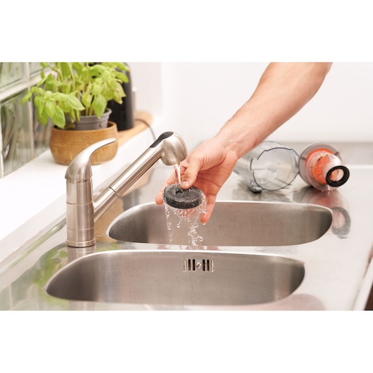 BLACKDECKER BHFEA18D1 vacuum filter being rinsed under faucet in kitchen sink, vacuum canister nearby.