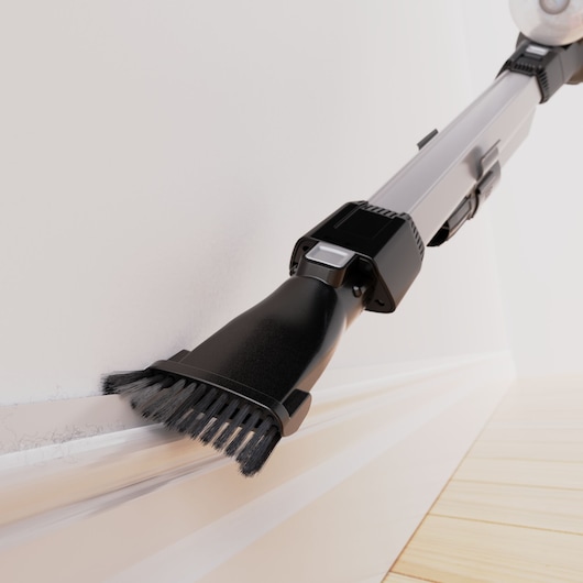 BLACKDECKER BHFEB520D1 vacuum cleaner close-up with brush attachment cleaning dust from white baseboard, photography.