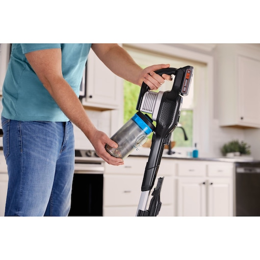 BLACKDECKER BHFEB520D1 stick vacuum in use, person emptying dust container in kitchen setting.