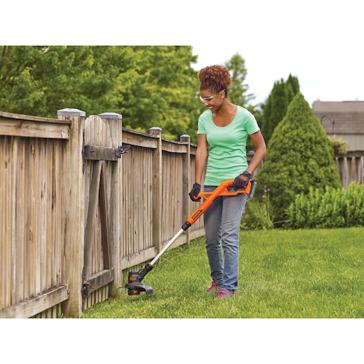 A woman is trimming grass using a BLACK+DECKER 20V MAX* String Trimmer/Edger, with new look powerconnect batery.