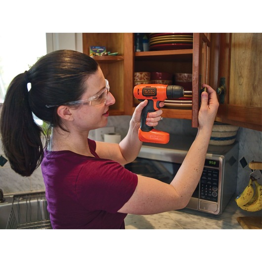 Photo of person using BLACKDECKER LD008 orange cordless drill to install handle on wooden kitchen cabinet.