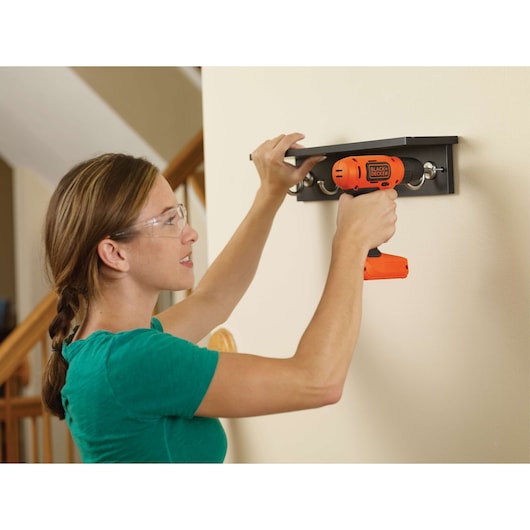 Photo of a person using a BLACKDECKER LD008 orange cordless drill to install a wall shelf indoors.